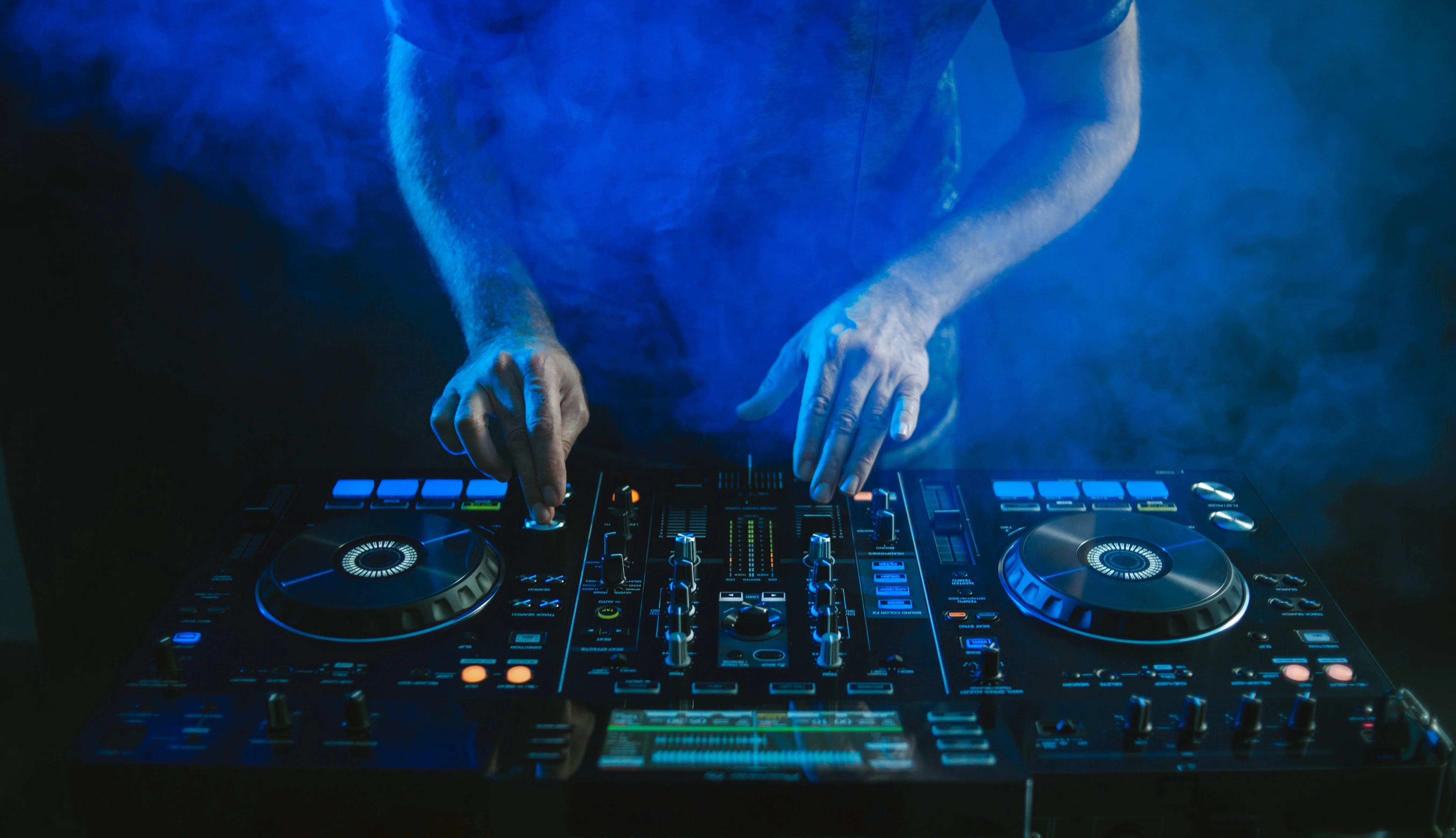 Closeup Of A Dj Working Under The Blue Lights Against A Dark Background In A Studio